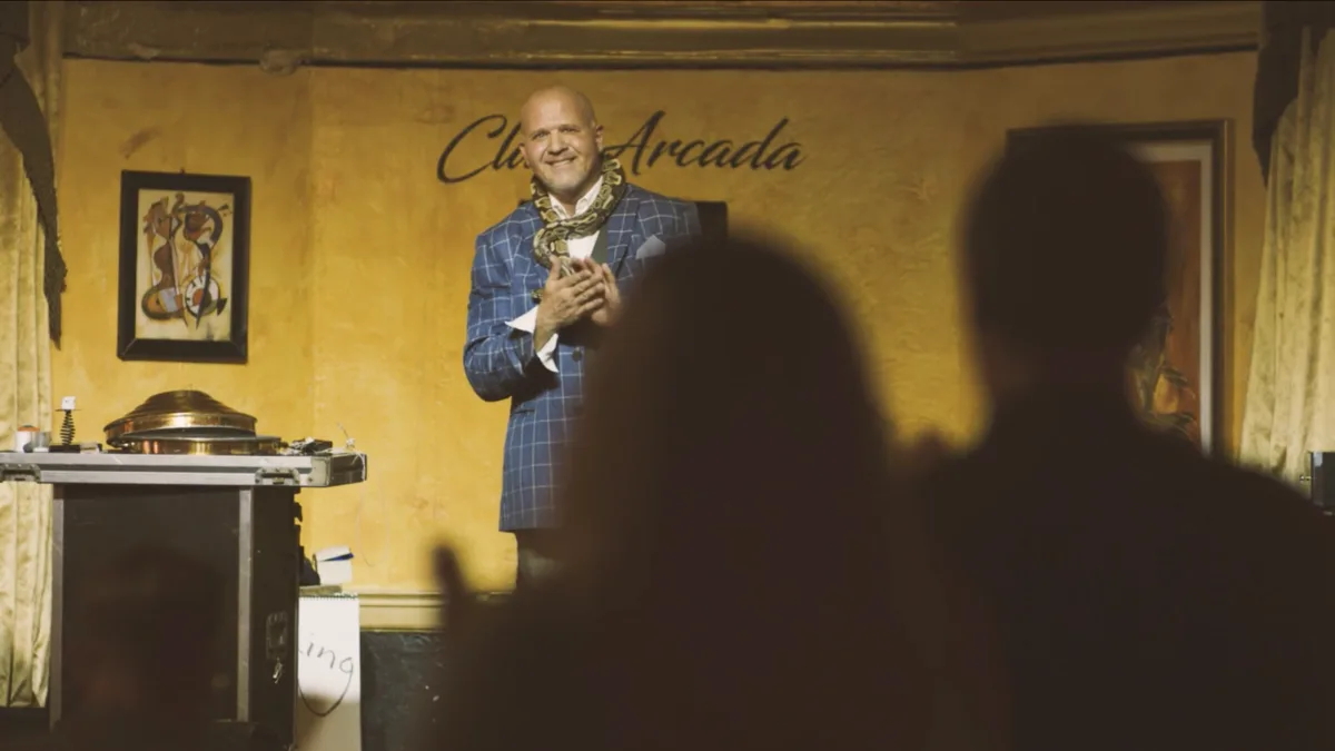 Mike DiDomenico on stage with a large snake around his neck, the audience standing to applaud in the foreground.