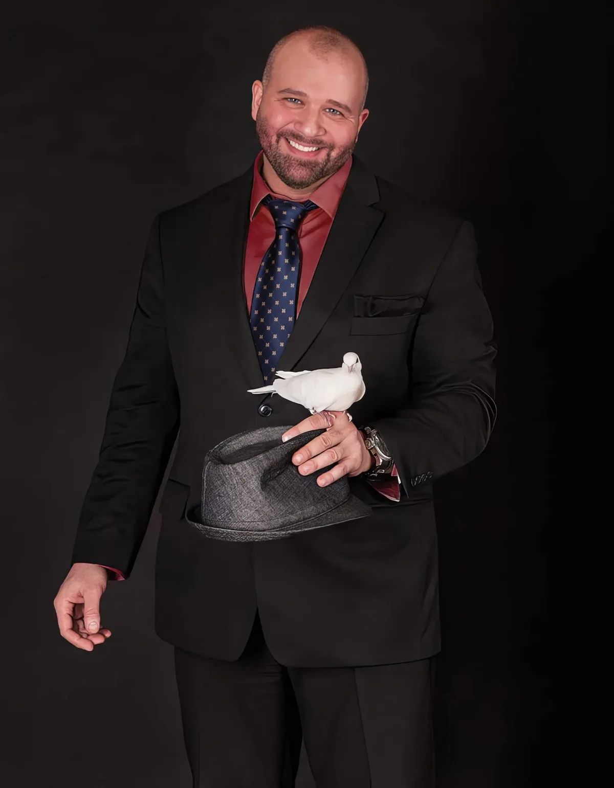 Mike DiDomenico in a dark suit holding a hat with a white dove perched on his hand.