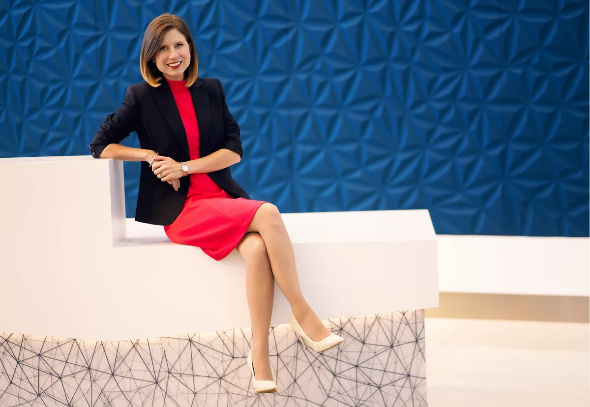 A headshot made on location against a sculpted blue wall, seated on a low white ledge.