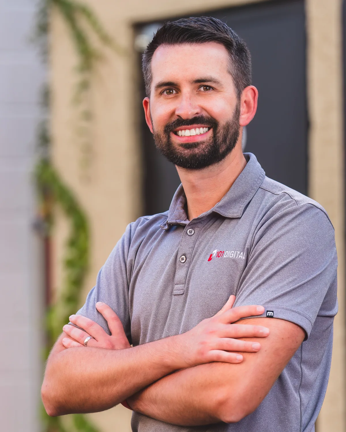 An on-site headshot in a company polo, arms folded, greenery and daylight filling the background.