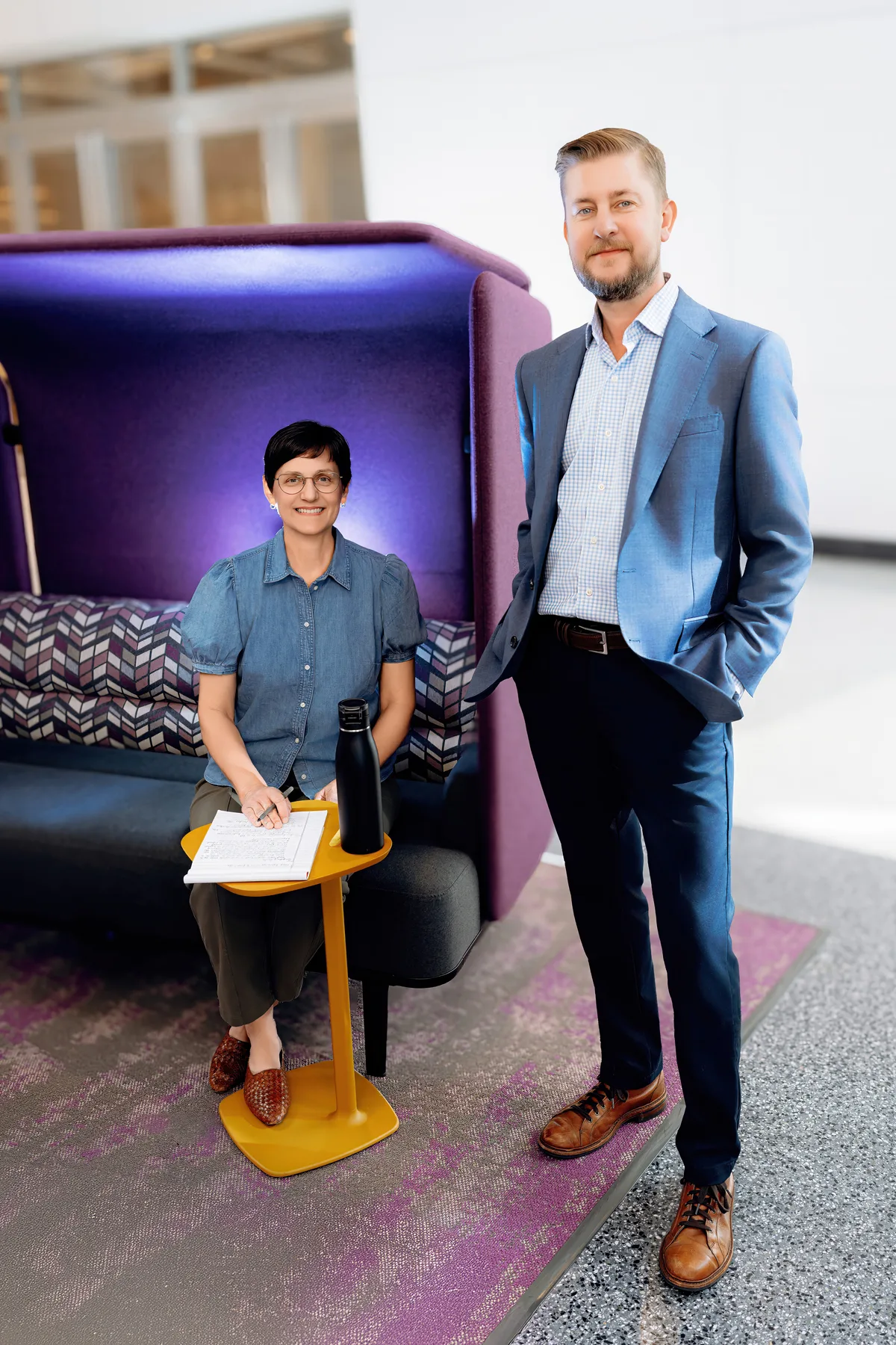 Two colleagues in conversation at a standing desk in a bright, modern workplace.
