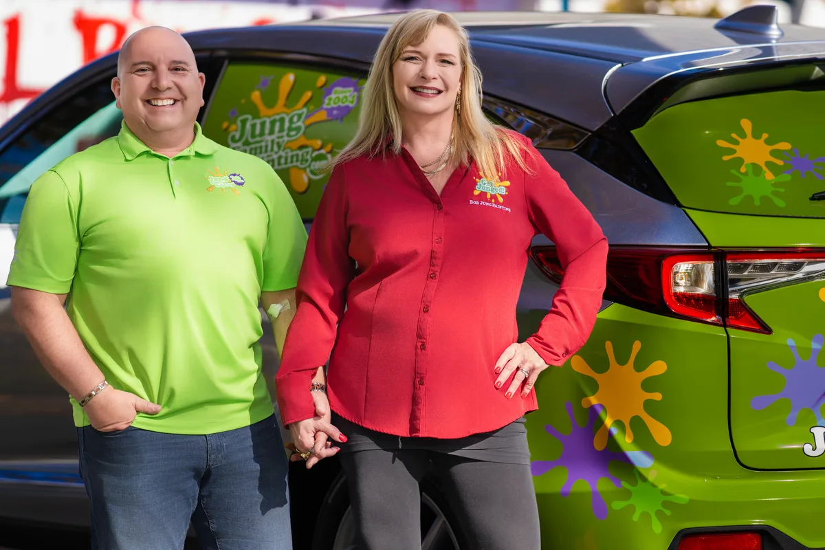 Two business owners standing beside their company car, its wrap covered in the bright artwork of their brand.