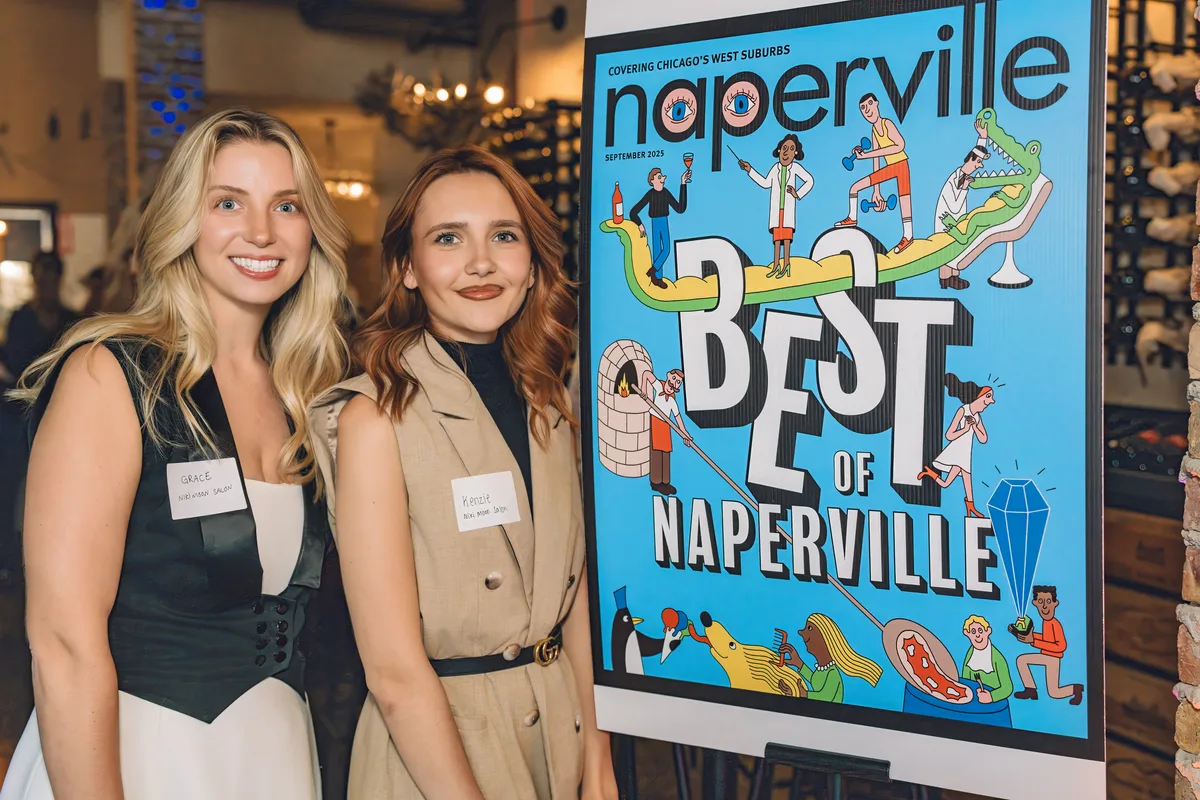 Two smiling guests with name tags beside an easel showing an illustrated Best of Naperville magazine cover.