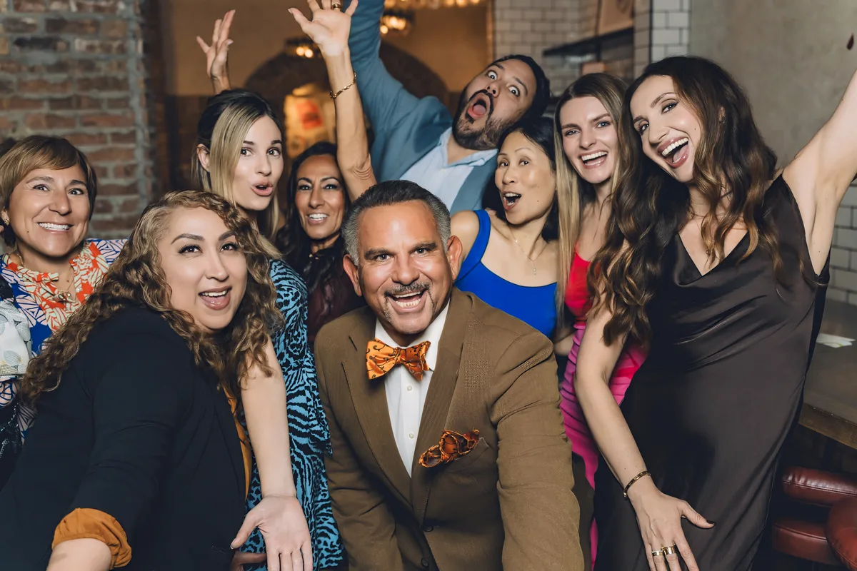 A group of guests cheering and mugging for the camera around a man in a bow tie at an evening party.