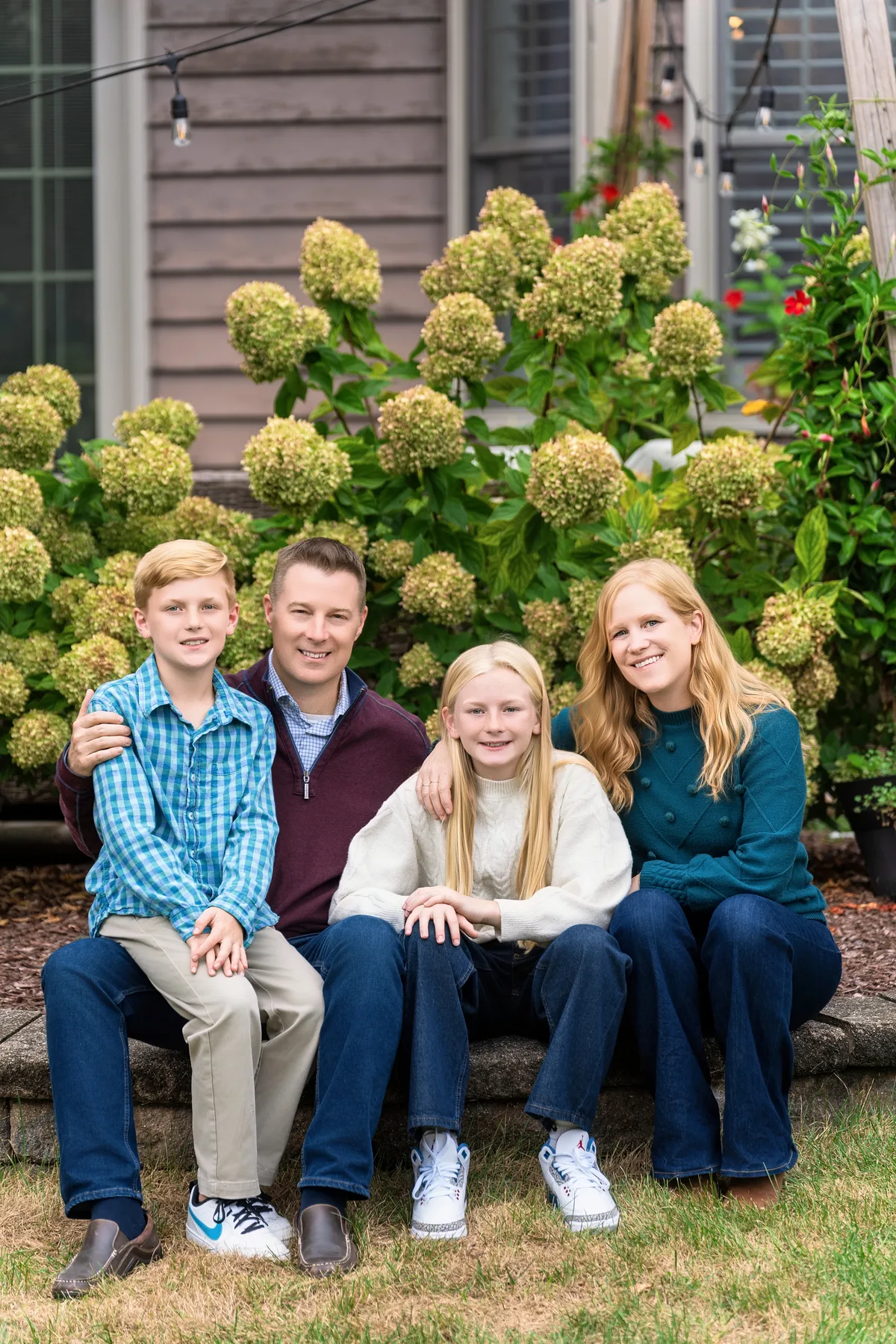 A family of four sits on a garden wall in front of hydrangeas in a Naperville backyard.