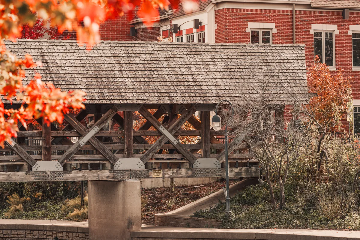 The covered bridge on the Naperville Riverwalk, red maple turning behind it.
