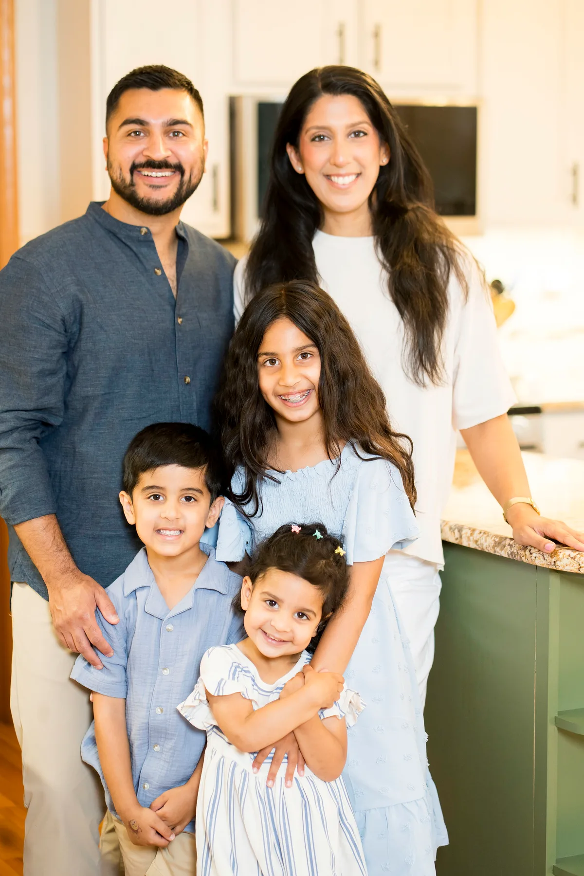 A family of five stands together at their kitchen island, the two youngest in front.
