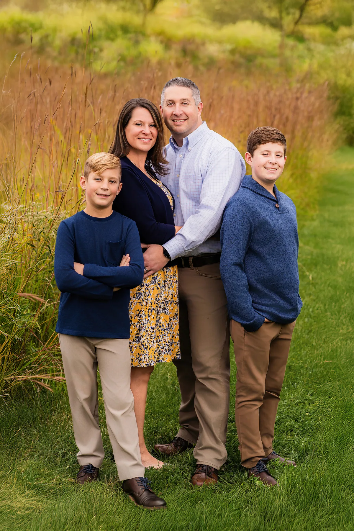 A family of four stands close together in front of tall prairie grass, the two boys on either side.