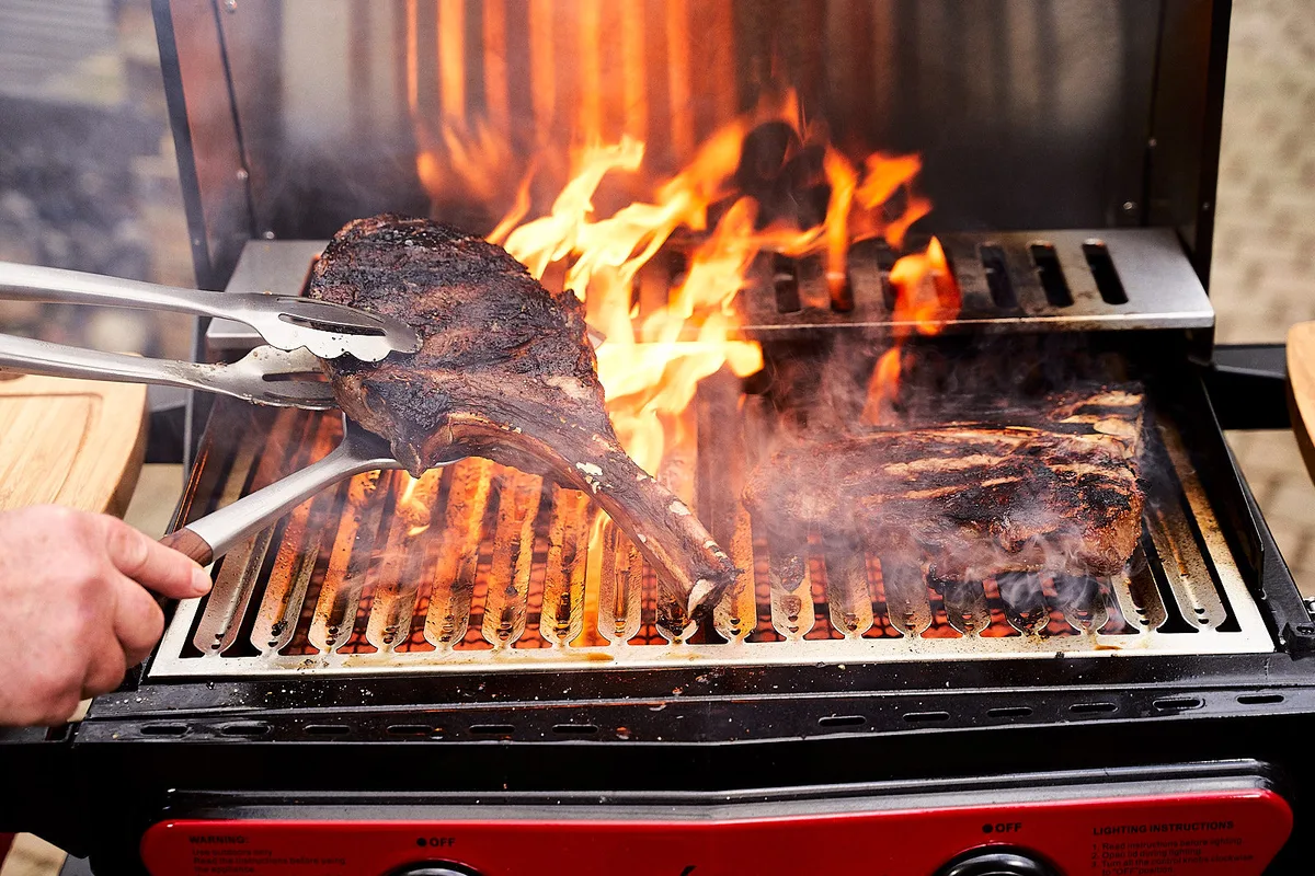 A steak over open flame on a grill, fire climbing through the grate.