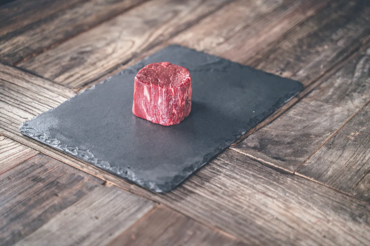 A raw filet mignon standing on a slate board on weathered wood.