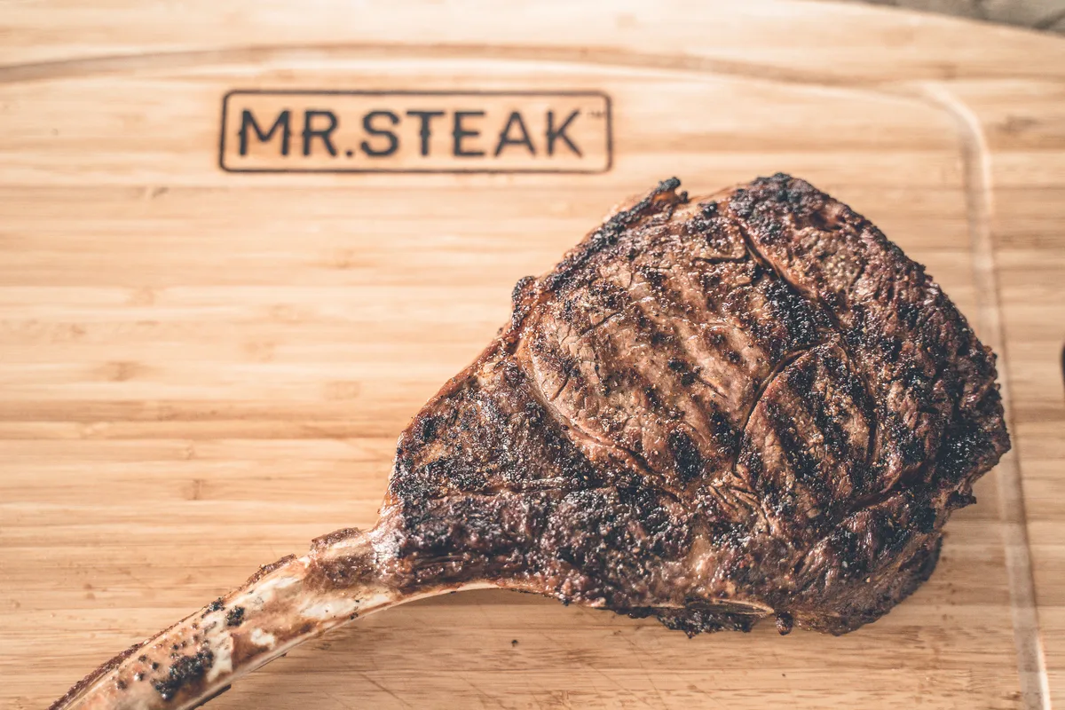 A grilled tomahawk steak on a cutting board branded Mr. Steak.