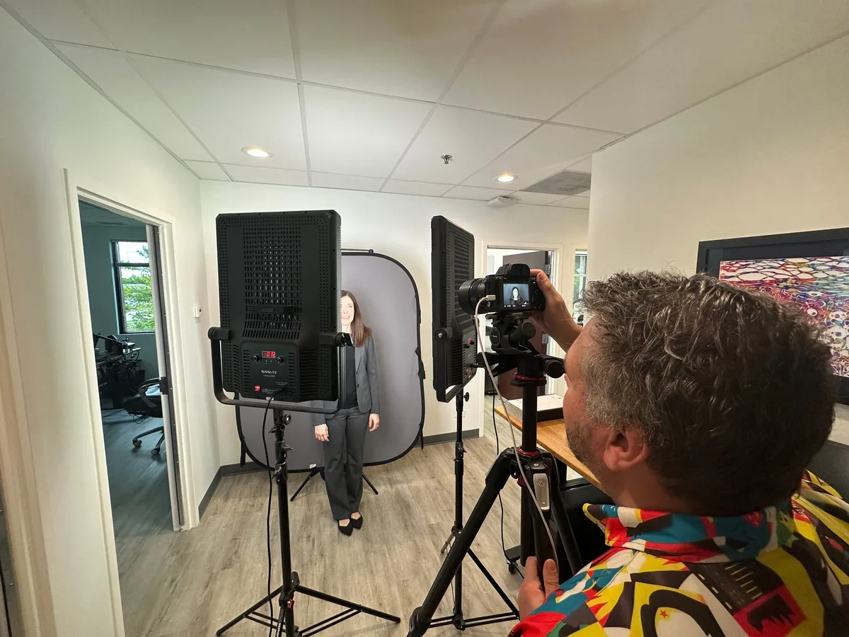 Over the photographer's shoulder: a woman on a gray backdrop between two LED panels, her image on the camera screen.