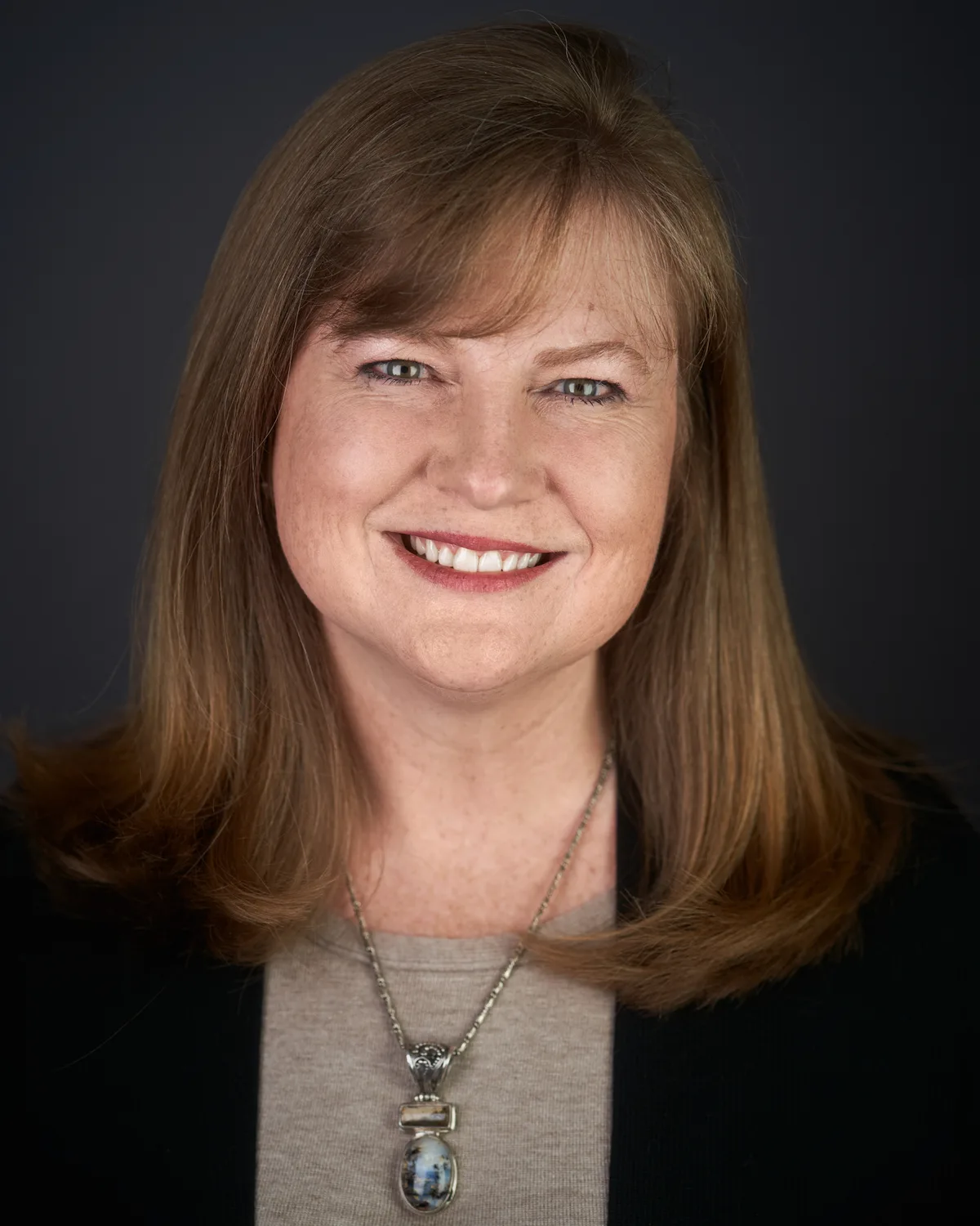 A headshot on a dark grey set, shoulders square to the camera, even light.