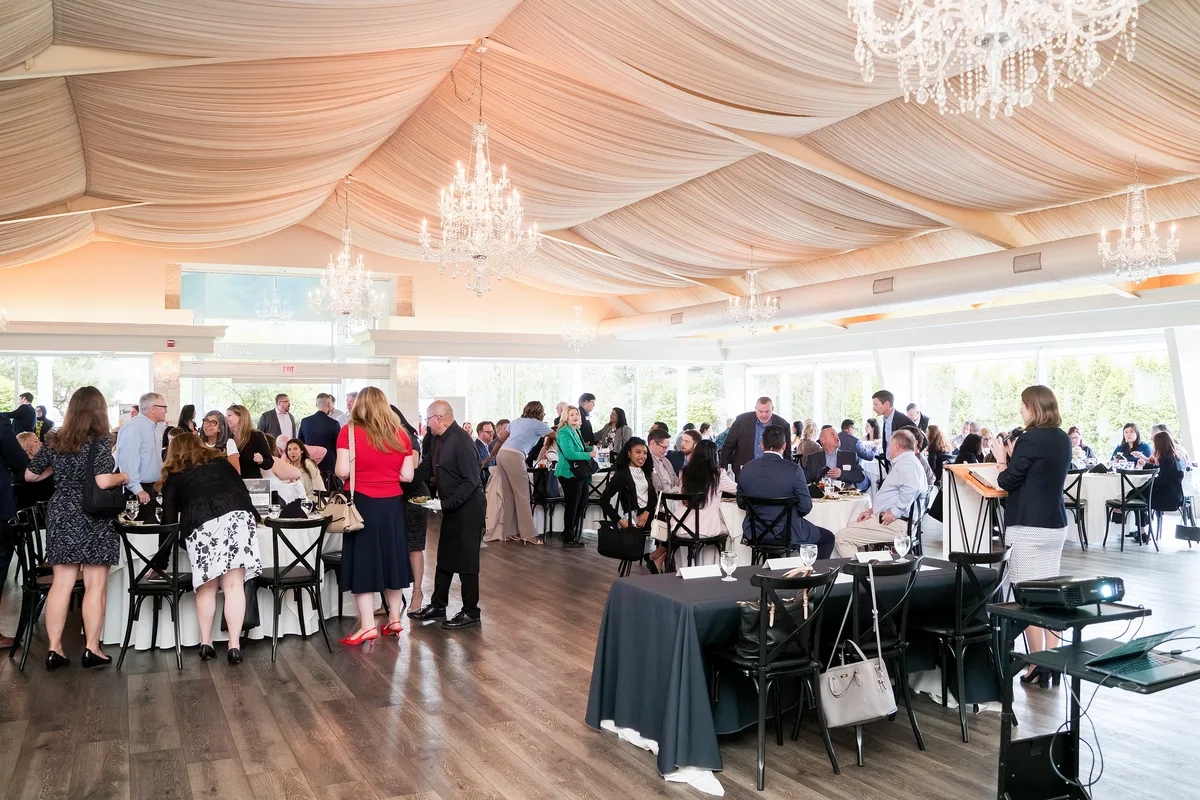A full banquet room of guests at a business luncheon in Naperville, tables set and conversation under way.