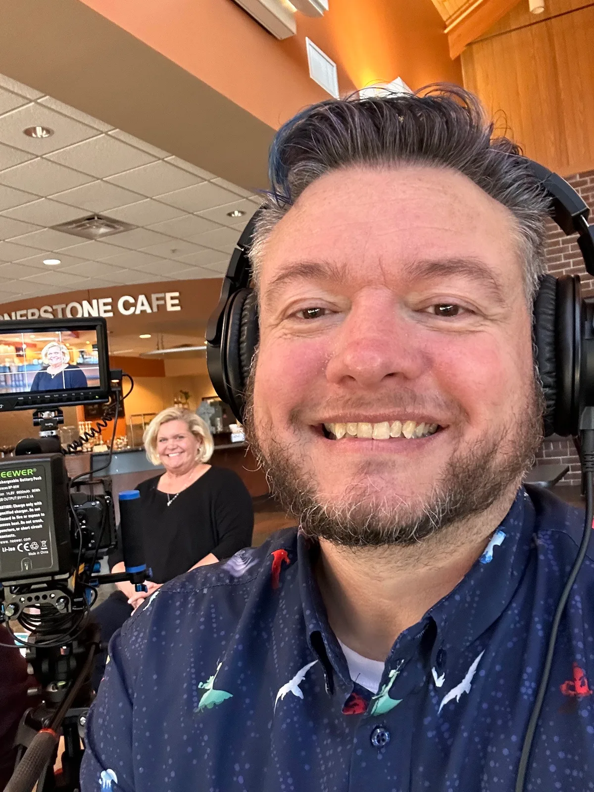 A camera operator in headphones beside a monitor showing the shot being recorded.