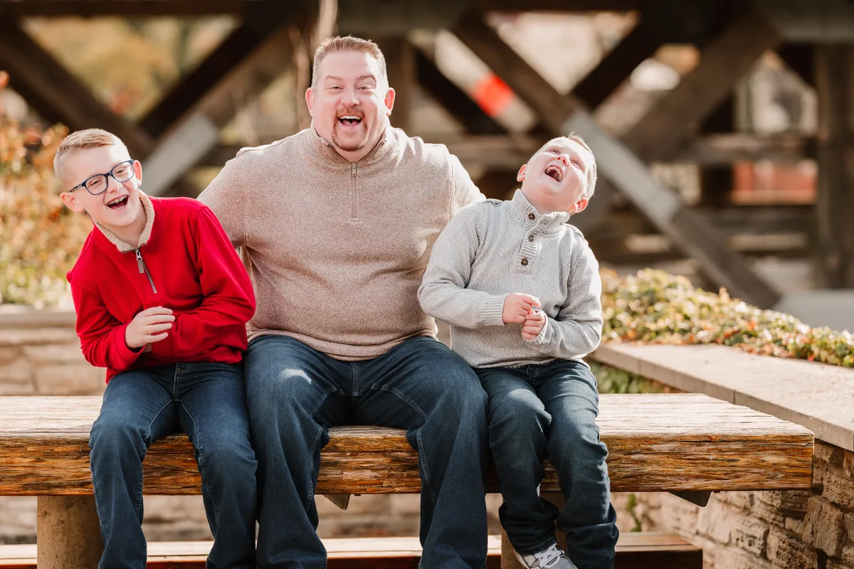 A father and two sons laugh together on a bench inside the covered bridge on the Naperville Riverwalk.