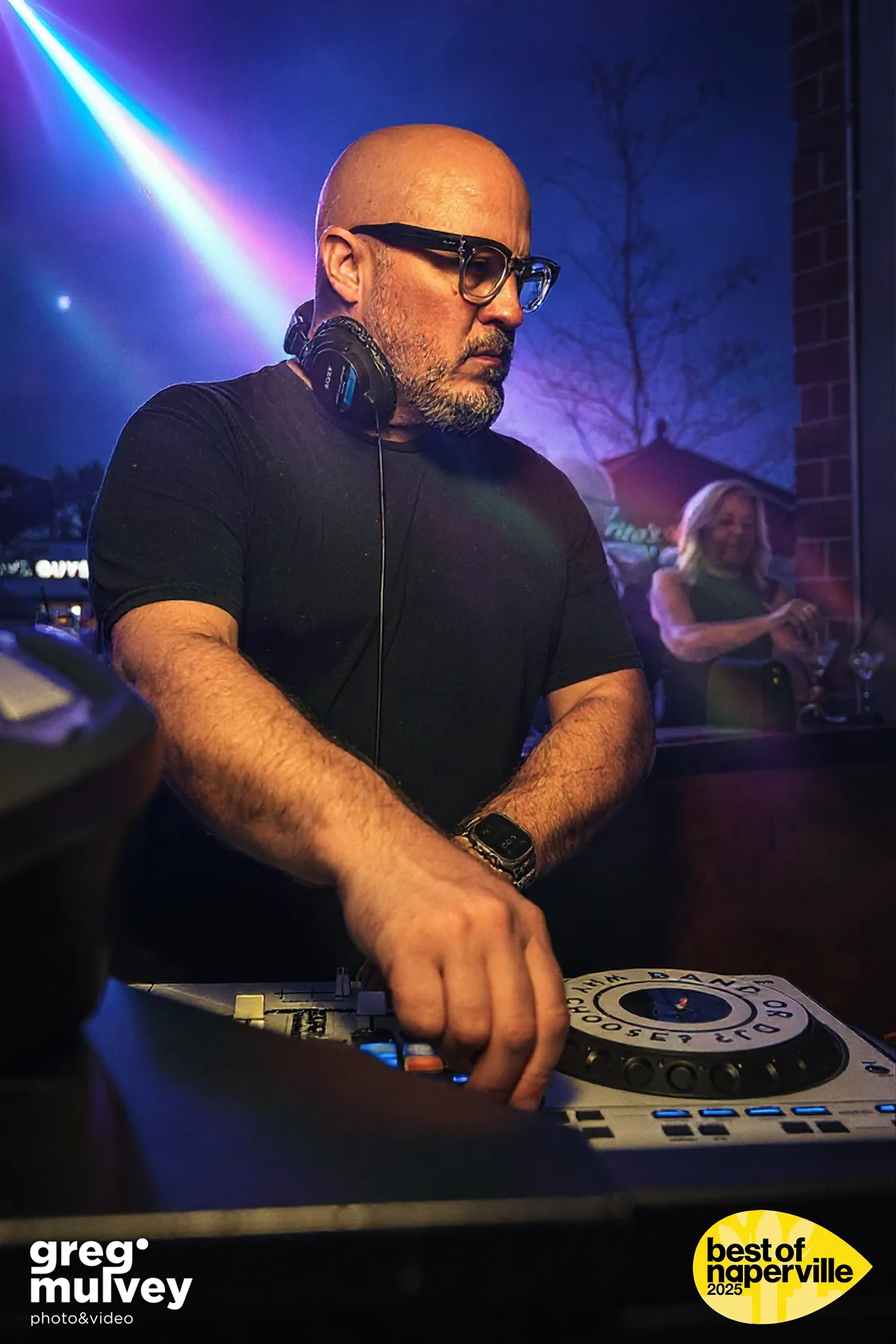 A DJ at the decks under blue stage light at an evening event.