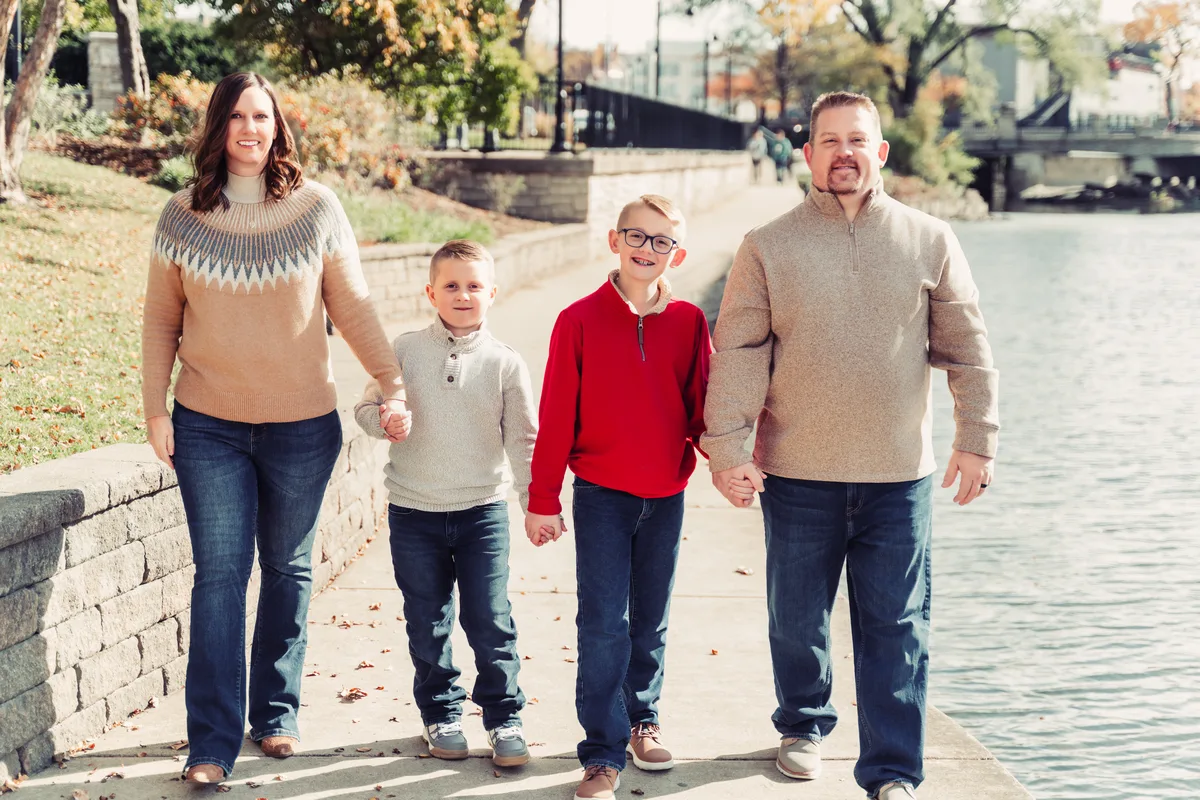 A family of four walks side by side along the Naperville Riverwalk on an autumn afternoon.