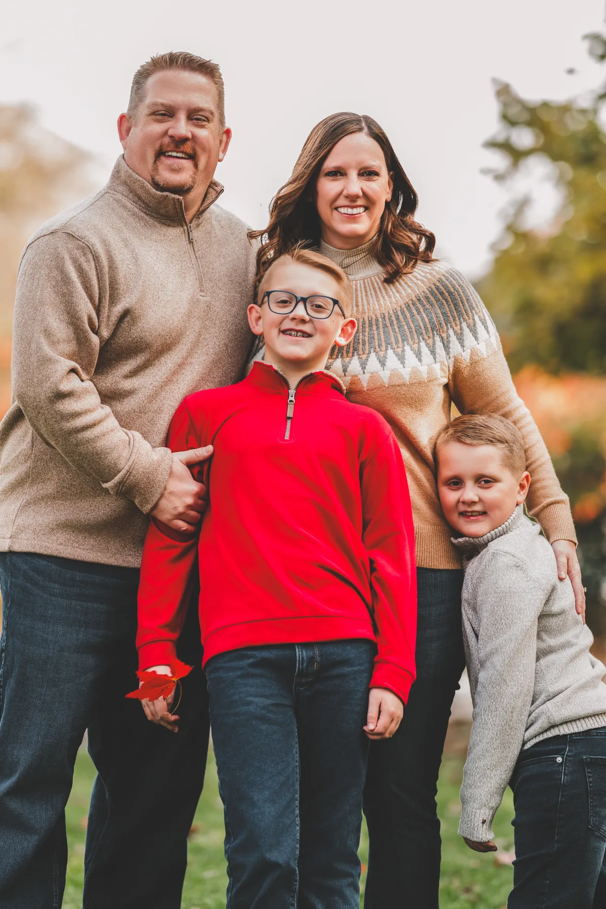 Parents and three children standing together outdoors in autumn light.