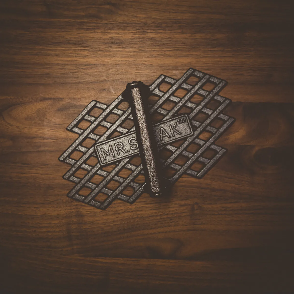 A cast iron grill mark press with a Mr. Steak handle on dark wood.