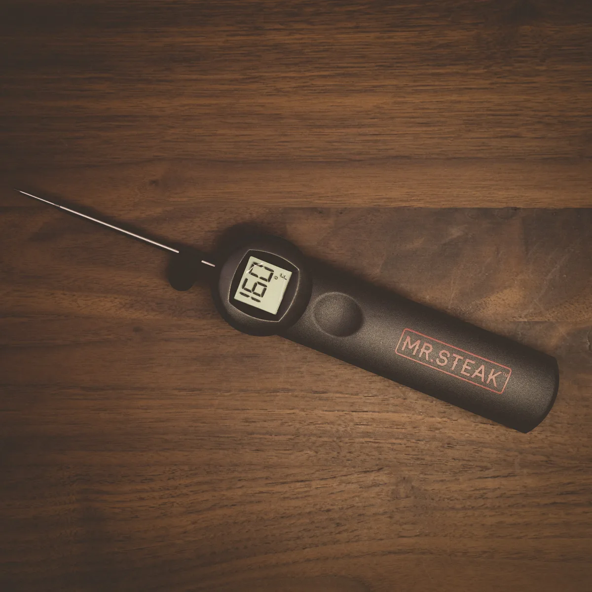 A Mr. Steak flip-tip digital meat thermometer on dark wood.