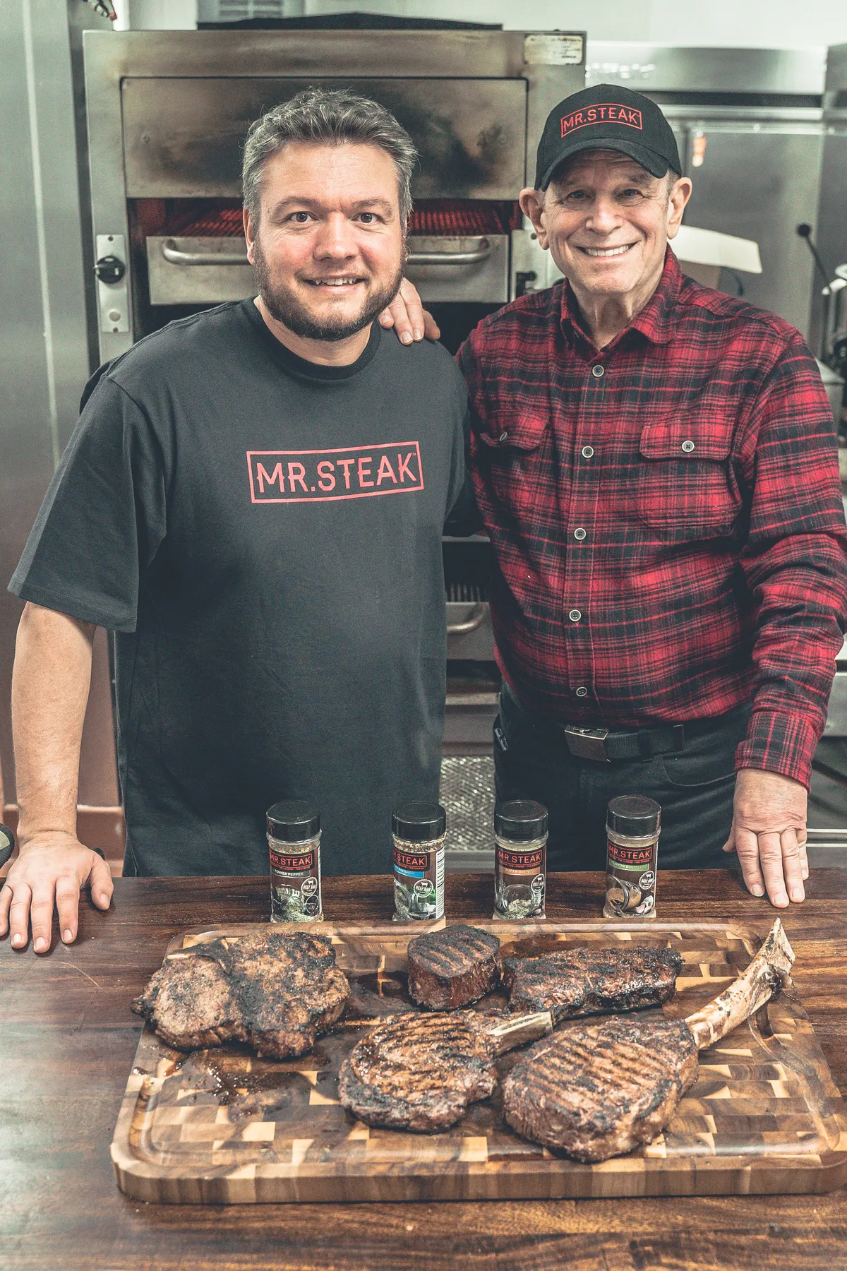 Greg Mulvey, left, and Mr. Steak's founder behind a board of grilled steaks in a commercial kitchen.