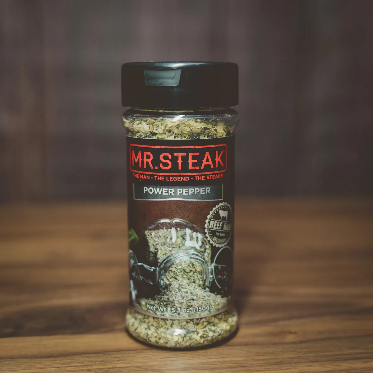 A Mr. Steak Power Pepper seasoning shaker on a wooden surface.